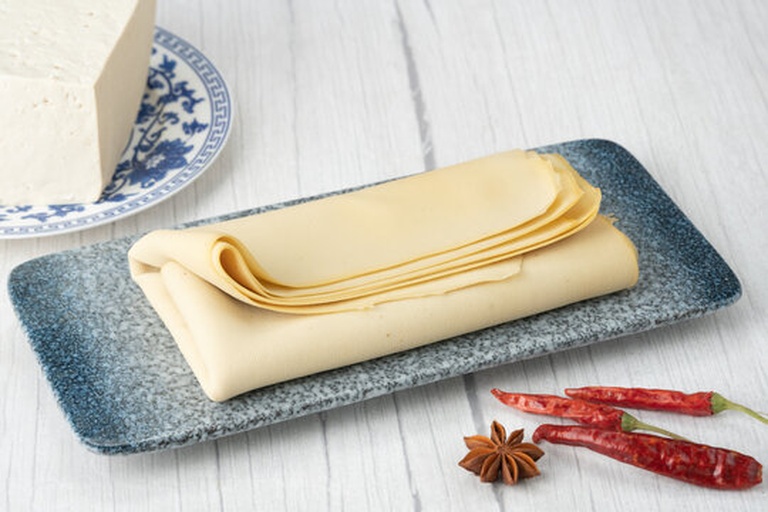 展示四种豆筋实物:左侧为金黄色油炸豆筋卷,中间为淡黄色非油炸素牛筋条,右上为薄片状豆皮,右下为红色包装的即食辣味豆筋零食,背景为木质厨房台面,旁边摆放 chopsticks 和小碟调料 豆筋的四种常见类型对比图