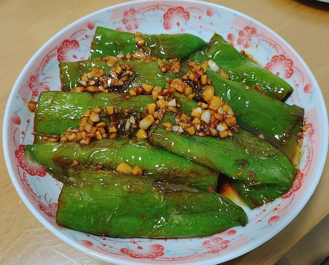 虎皮红椒成菜特写：深红油亮的红椒整齐卧于青花瓷盘中，表皮褶皱清晰如虎纹，边缘微翘带焦脆感，点缀金黄蒜末与翠绿葱花，盘底有琥珀色酱汁反光