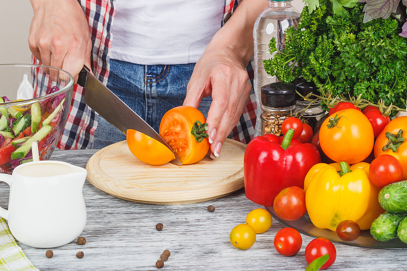 一位女性在厨房中正在将切好的青瓜和西红柿放入玻璃搅拌机中