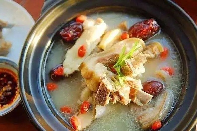 一碗热腾腾的西洋参猪骨汤,汤色金黄,猪骨与西洋参片清晰可见,旁边配有小碟枸杞和红枣 西洋参猪骨汤成品图