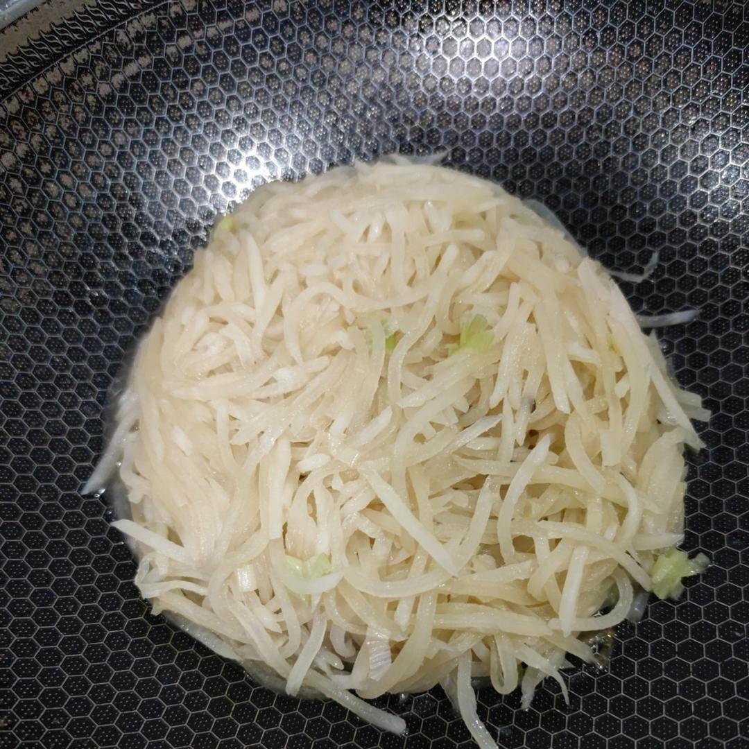 正在翻炒的大红皮萝卜丝,锅中热气腾腾,萝卜丝呈半透明状,锅具为中式炒锅,背景为厨房环境 炒制大红皮萝卜过程