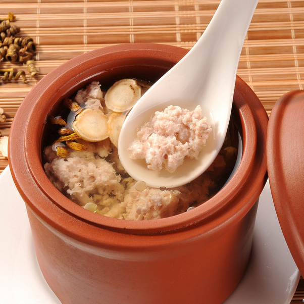 一口陶瓷砂锅正在炉火上慢炖,锅内翻滚着乳白色的鹿鞭羊肉汤,可见鹿鞭段、羊肉块、枸杞和姜片,蒸汽升腾,旁边摆放着原始干鹿鞭和中药材,展现从原料到成品的过程 鹿鞭炖汤烹饪过程