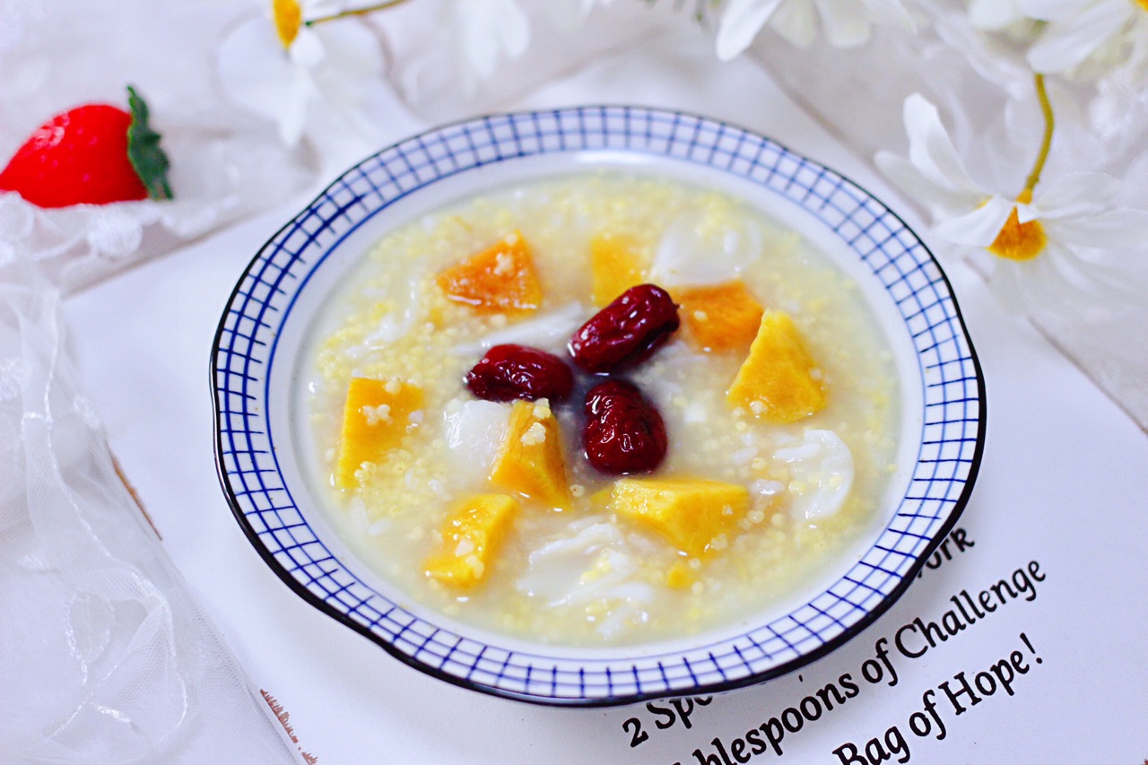 一碗热气腾腾的南瓜小米粥,金黄色泽明亮,表面有轻微油光,碗边点缀几粒完整的金黄小米,南瓜块软烂融入米汤中,背景为木质餐桌与原木色餐具,营造温暖养生氛围 南瓜小米粥特写