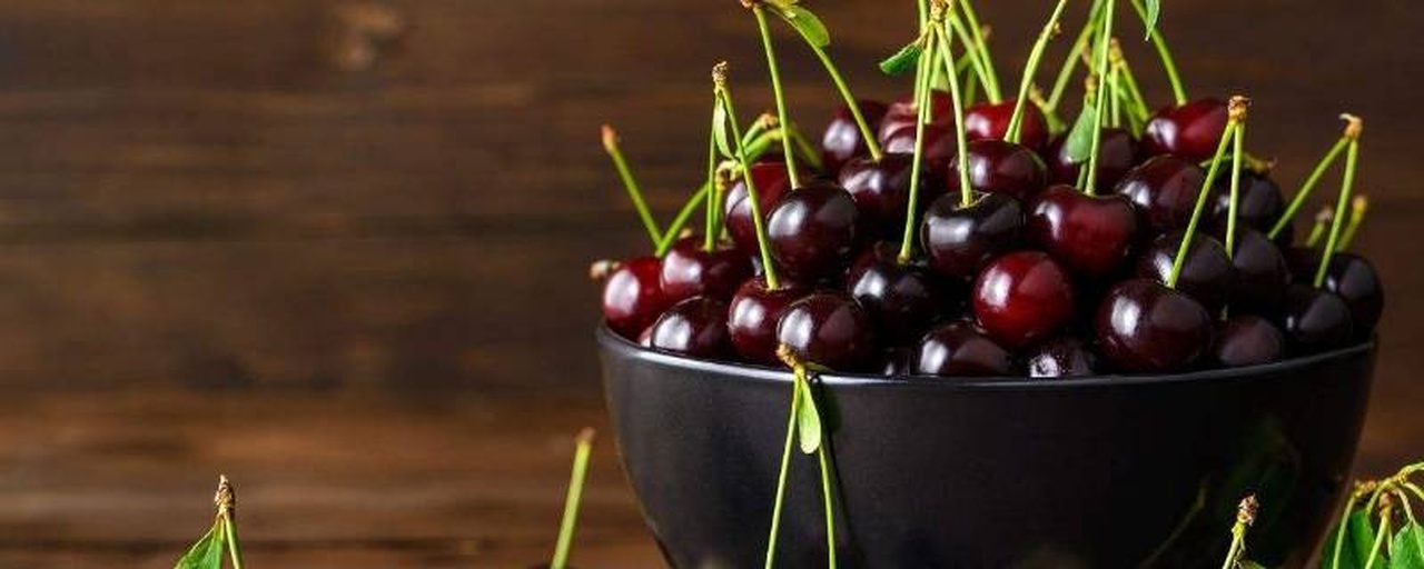 家庭厨房中透明玻璃碗盛放新鲜带梗车厘子，旁边放置柠檬片