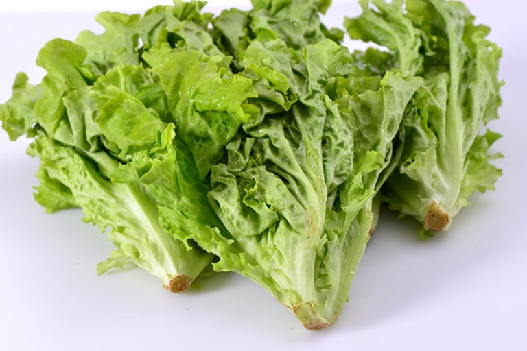 新鲜翠绿的整根莴苣放在木质砧板上，表皮光滑，叶子鲜嫩，背景为厨房台面