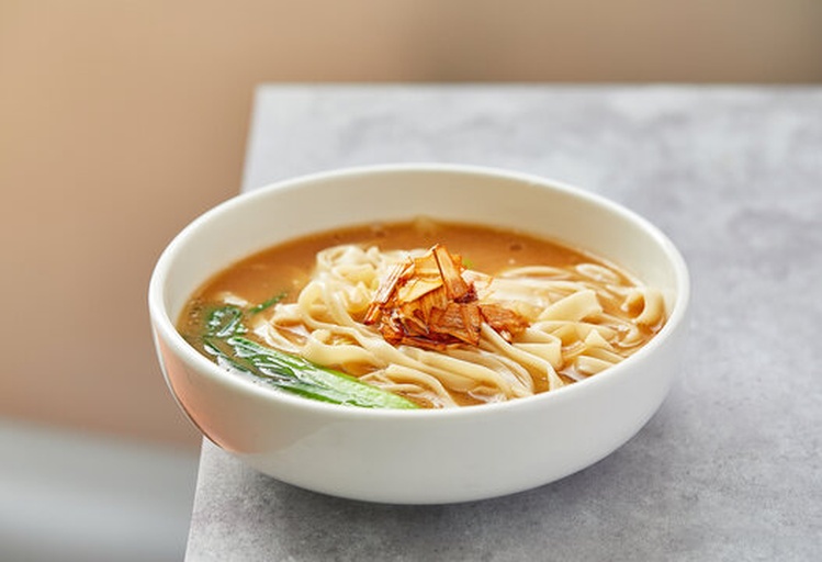 现代餐厅中,顾客正在享用一碗装在精致碗中的姜汤面,旁边摆放着品牌宣传册和姜汤系列产品 现代姜汤面餐厅场景