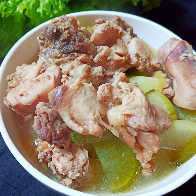白瓷碗中盛满冬瓜炖鸡汤,汤色清亮微乳白,冬瓜块晶莹剔透,鸡肉块分布其间,表面浮有零星油珠和葱花点缀,旁边配有木筷和小碟,呈现温馨家常用餐氛围 成品盛装效果