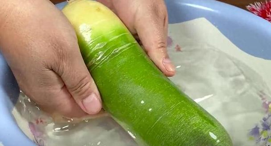 一位家庭主妇正在厨房水槽中用手清洗一把刚从萝卜上摘下的绿色萝卜缨,水珠溅起,背景可见切好的萝卜块和砧板,展示日常处理过程 家庭厨房中清洗萝卜缨的场景