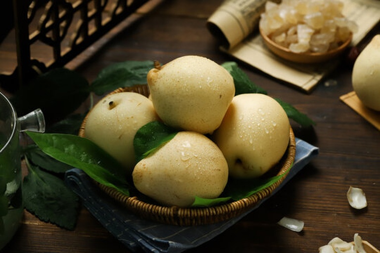 一份精致摆盘的南果梨雪糕,白色雪糕球置于玻璃碗中,表面微微融化,周围点缀薄荷叶和南果梨切片,背景为木质餐桌与阳光洒落的窗台,整体风格清新自然 成品南果梨雪糕多角度展示