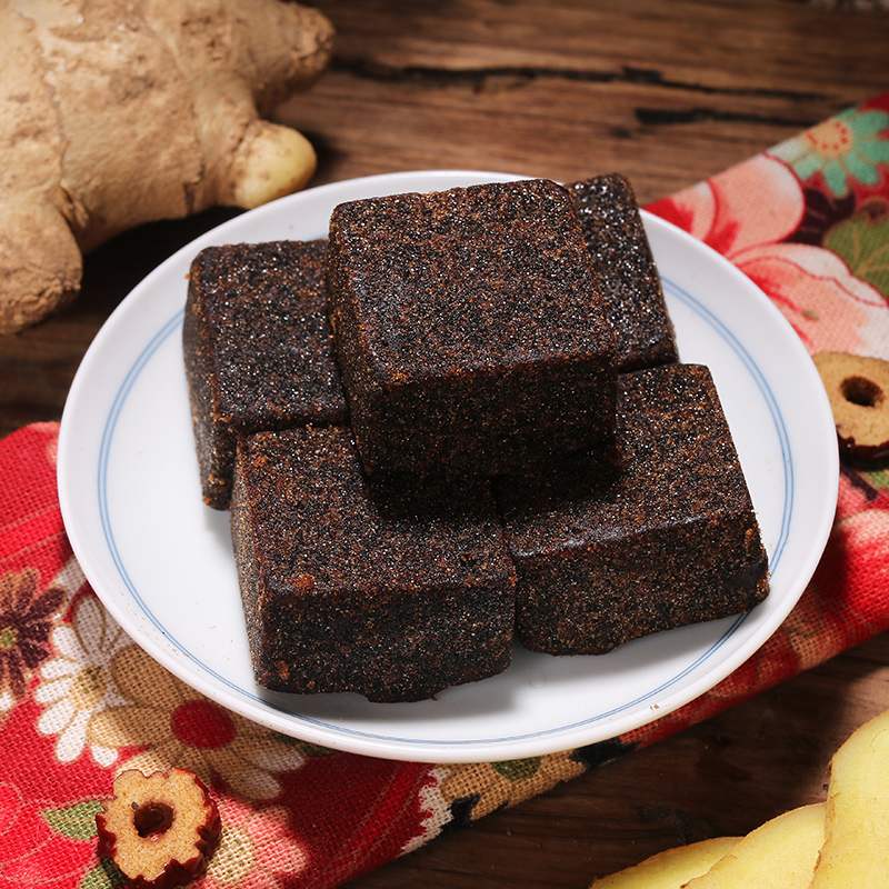 姜母四物红糖成品特写：深琥珀色膏体表面可见细密姜母纤维丝，质地柔韧不粘手，置于青花瓷碗中，旁边放置温度计显示42℃（模拟人体温服状态）