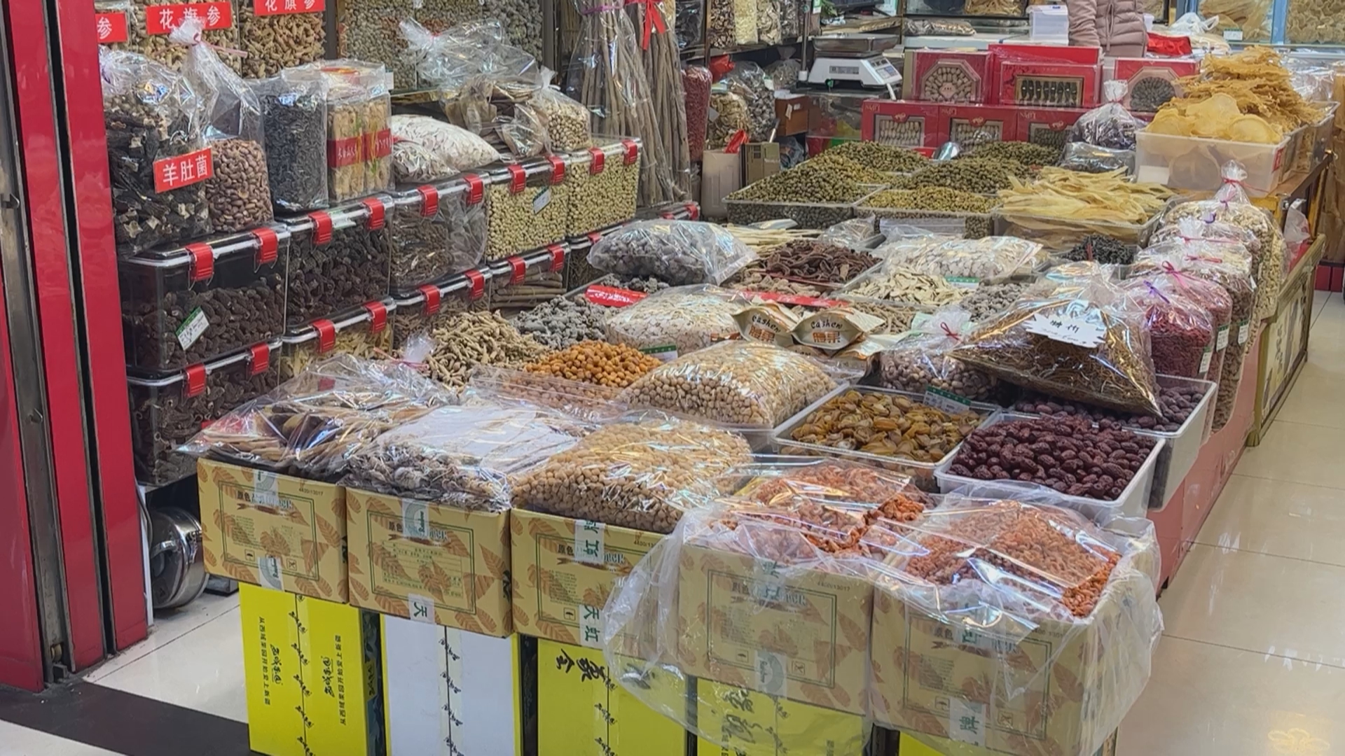 一个传统的露天集市场景,木质摊位上摆放着多种中药材和干植物,中央位置有一束扎好的干柚子叶,标签清晰写着‘柚子叶’,摊主正在向顾客介绍产品,周围环境充满生活气息 集市上摆满干草药的摊位,中间一捆标有“柚子叶”的干燥植物