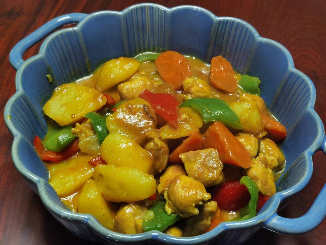 新鲜鸡腿肉、黄皮土豆、洋葱、胡萝卜整齐摆放在砧板上,旁边有咖喱块和调味料瓶罐,背景为厨房操作台 食材准备图