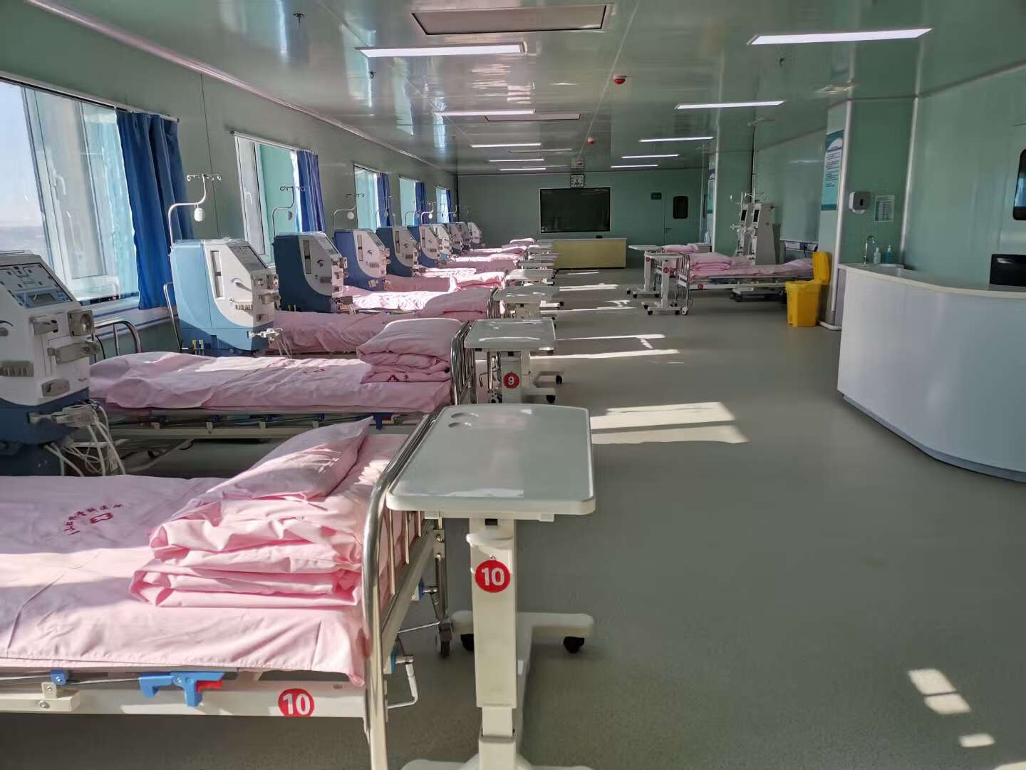 一位中年男性透析患者在厨房操作台上用刀切黄桃,旁边放着一碗清水用于浸泡果片,台面上还有电子秤和记录本,墙上挂着血压计,整体环境整洁温馨 透析患者在家准备水果