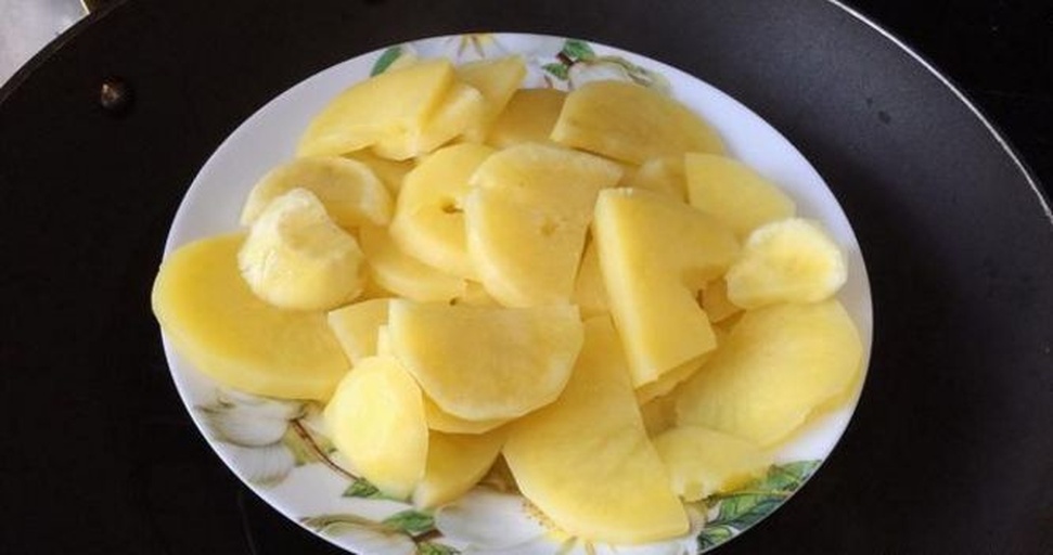 一盘刚蒸好的金黄色土豆块被倒入碗中,厨师正用压泥器将其碾压成细腻顺滑的土豆泥,旁边摆放着黄油块和牛奶瓶,背景为厨房操作台 土豆蒸熟后压成泥的过程