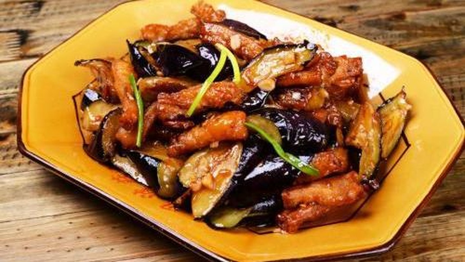 红烧茄子特写：深紫色茄块裹着琥珀色酱汁，表面微泛油光，配青椒片与蒜末，盛于白瓷浅盘中