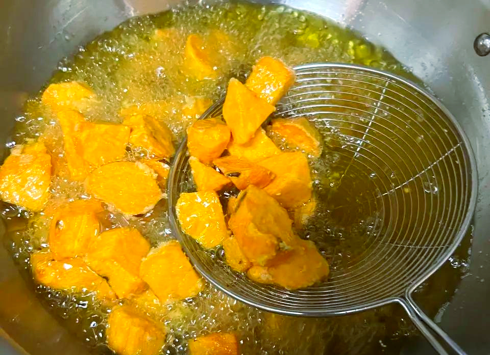 一口黑色铁锅中正在油炸脆皮冬瓜,几片裹着金黄面衣的冬瓜片漂浮在热油中,表面泛起细密气泡。背景可见温度计显示油温为165℃,操作者手持竹筷轻轻翻动食材 脆皮冬瓜油炸过程图