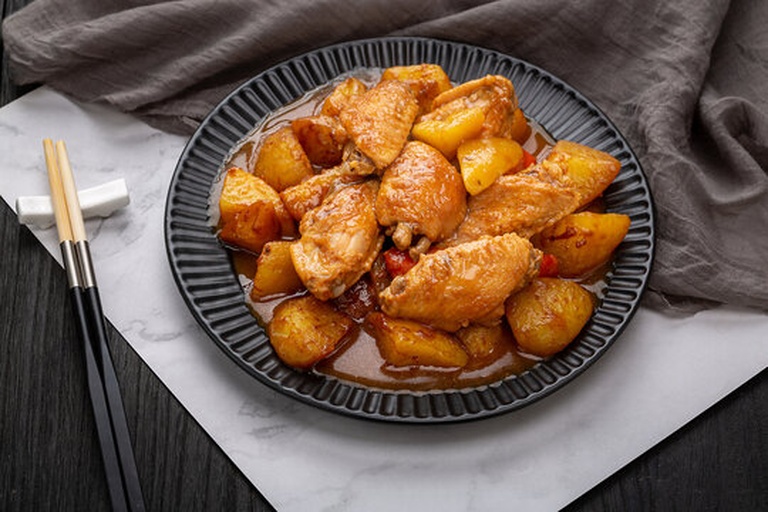 一锅正在炖煮的红烧鸡翅与土豆,汤汁浓稠,鸡翅呈棕红色,土豆块半透明状,表面裹满酱汁,锅边微微冒泡,热气腾腾,背景为木质厨房台面 红烧鸡翅与土豆混合炖煮的特写镜头