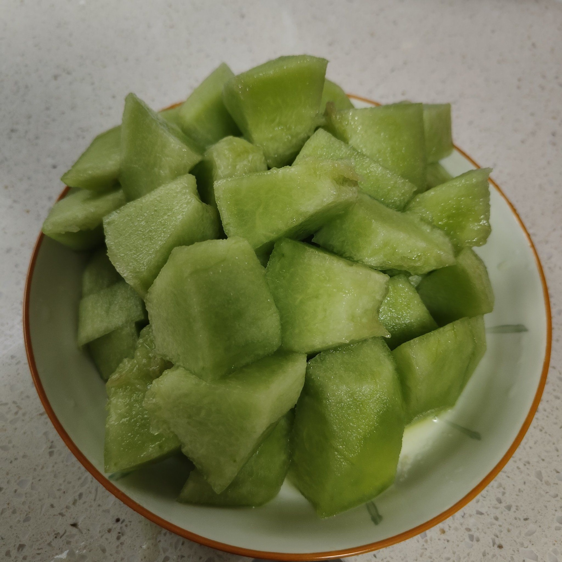 一个切块的哈密瓜与其他水果(如蓝莓、草莓、猕猴桃)共同摆放在白色瓷盘中,旁边有一小碟坚果,整体呈现健康饮食搭配理念,背景为自然光线下的厨房台面 哈密瓜与水果拼盘搭配图