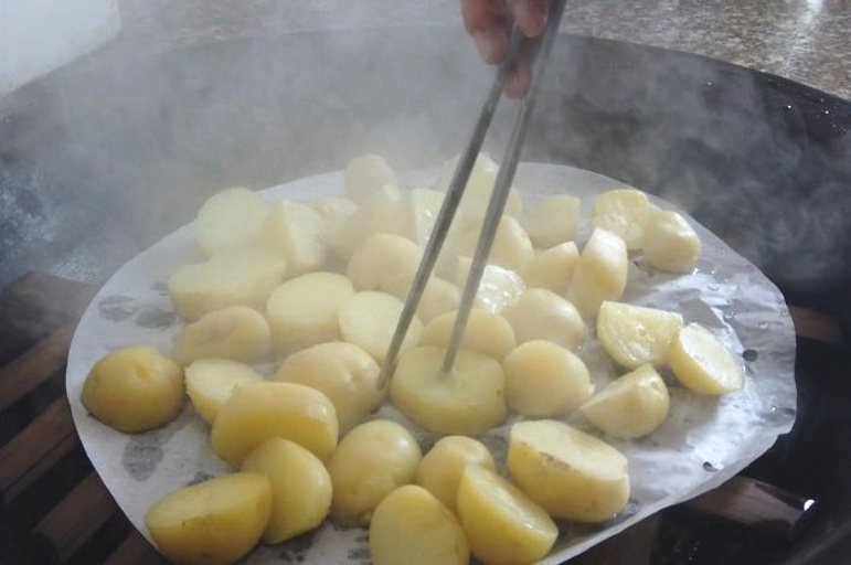 家庭健康土豆烹饪实景:突出蒸制工具、带皮完整土豆、零添加调料组合,体现可复制、易执行的家庭实践方案 家庭厨房场景:不锈钢蒸锅内整齐码放带皮土豆,锅盖微启透出热气,台面铺亚麻布,旁置竹制料理盘盛放刚出锅的土豆、小葱、蒜末、陈醋——呈现健康家常烹饪过程