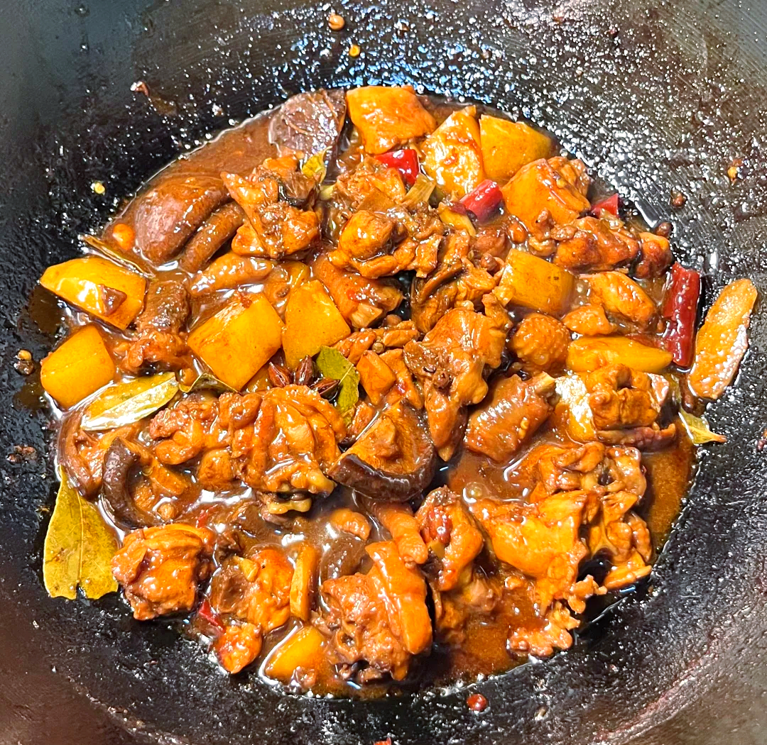 砂锅中盛着金黄色的老母鸡炖土豆，汤汁浓稠，鸡肉块分明，土豆软糯，表面撒有绿色葱花，热气腾腾