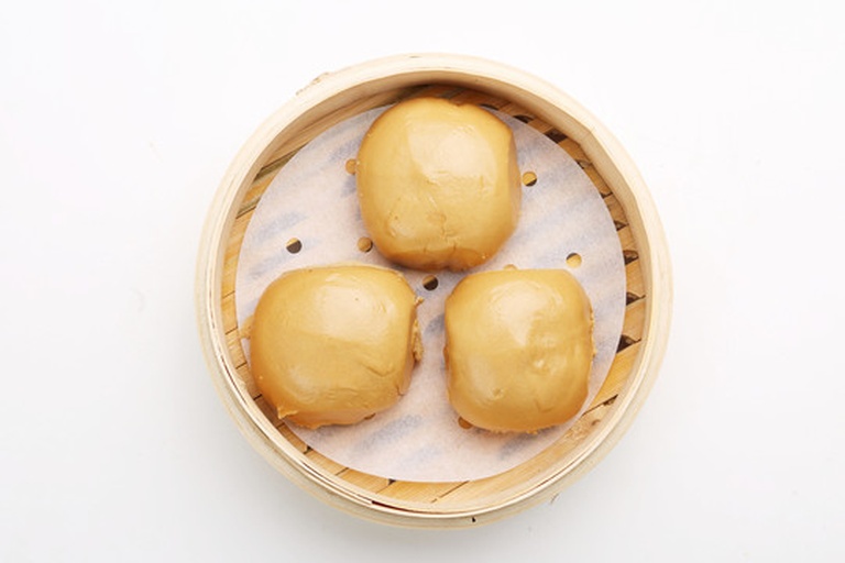 多个青绿色调的窝窝头生坯整齐排列在竹制蒸屉上,底部有圆形纸垫,窝窝头呈上宽下窄的喇叭状,中心有明显孔洞,表面略显颗粒感,体现粗粮质感 青萝卜窝窝头生坯摆放