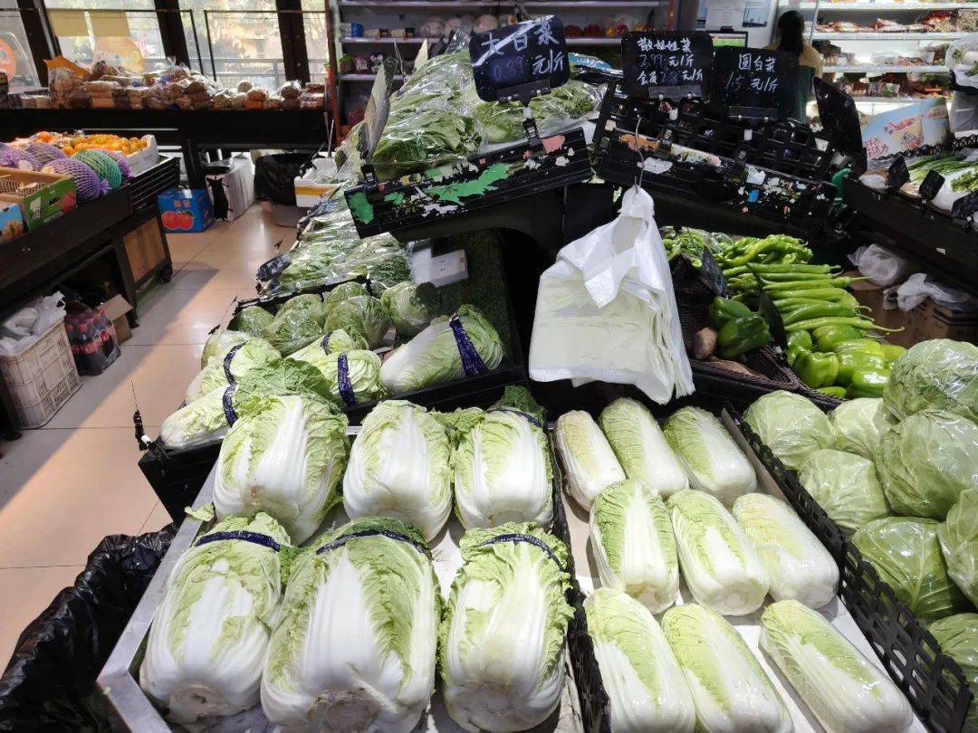 现代超市生鲜区货架,左侧为透明塑料盒装的黄色娃娃菜,标签标注‘金黄甜糯’‘富含胡萝卜素’;右侧为托盘覆膜的绿色娃娃菜,标价更低,背景有消费者正在挑选,体现终端消费场景差异 绿色与黄色娃娃菜在超市货架上的陈列对比