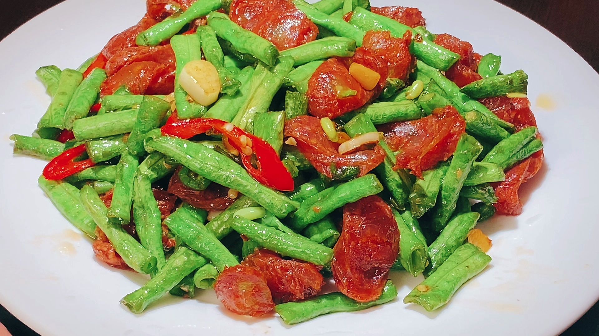 高清特写:左侧为已摘筋斜切的鲜嫩四季豆段(翠绿饱满,断面水润);右侧为温水浸泡后吸干水分的广式腊肠薄片(肥肉微透、瘦肉粉红、边缘整齐无碎屑),背景为冰水浸泡中的四季豆,水面浮着细小气泡,体现‘激冷固脆’工艺 四季豆与腊肠预处理对比图