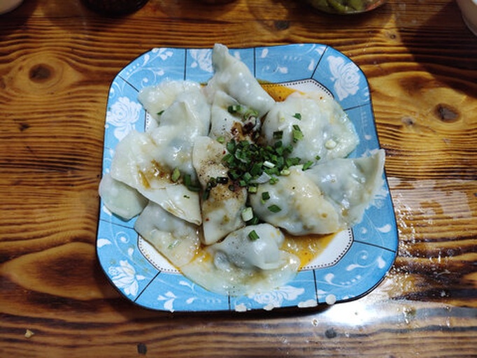 一间明亮的餐厅内,一家三口围坐在木桌旁,桌上摆着一盘热气腾腾的白色饺子,每人面前都有小碟蘸料,孩子正夹起一个饺子开心地笑着,背景墙上挂着中国风装饰画 一家人围坐餐桌享用香芹饺子的温馨场景