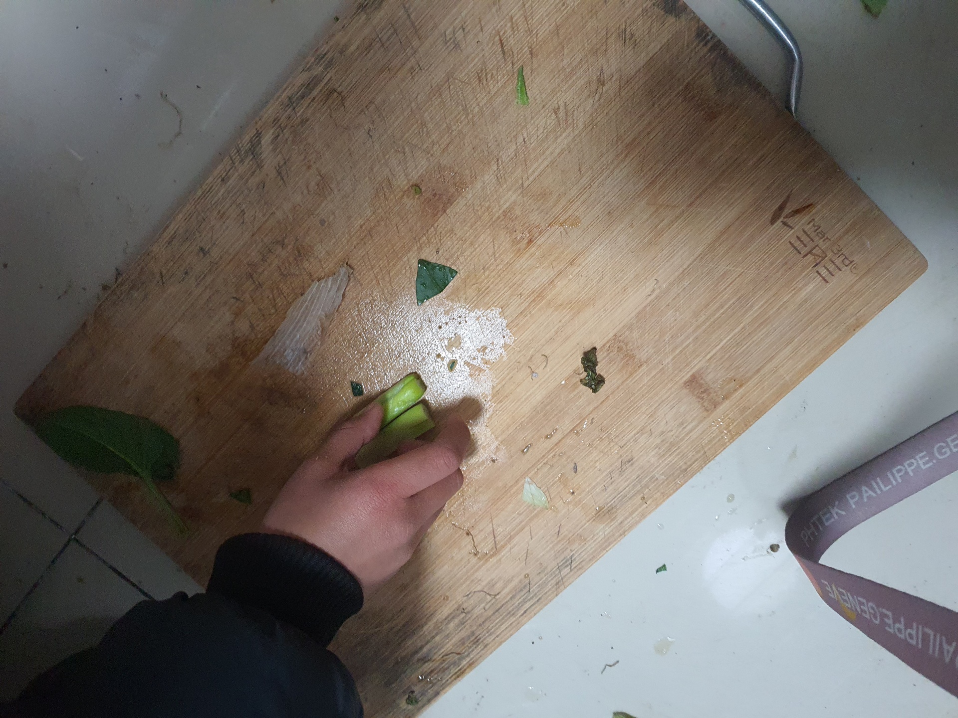 厨房场景中,一只手正在用流水冲洗摊开的生菜叶片,另一只手持刀准备切配,台面上有盐罐和小苏打瓶,背景为干净的料理台 家庭清洗生菜操作实景图
