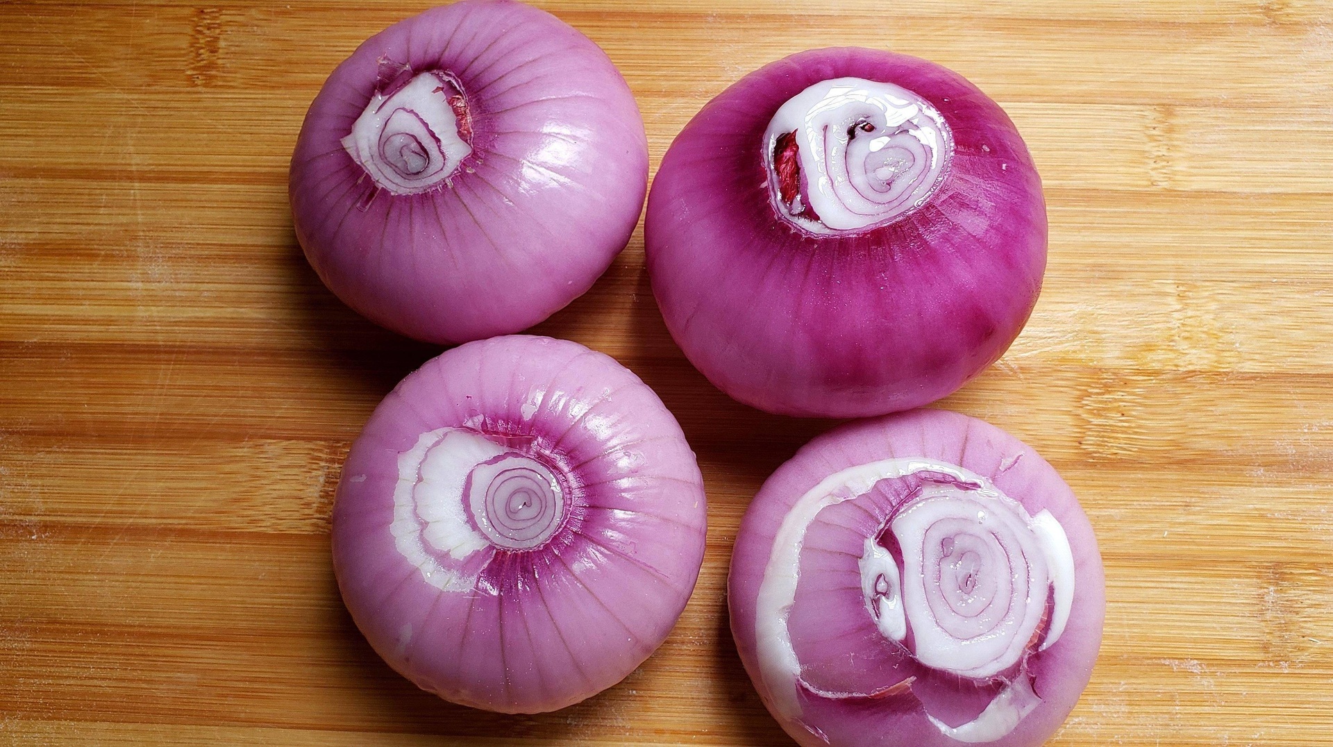 一个新鲜的白色洋葱被横向切开,露出层层分明的肉质结构,边缘透明微带粉红,中心可见尚未完全发育的芽点,背景为木质砧板,旁边有一把不锈钢厨刀 洋葱横切面特写