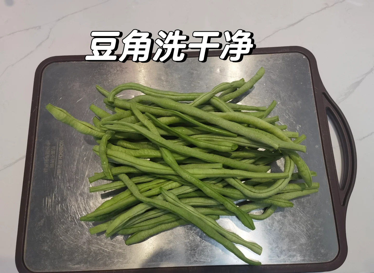 一名厨师正在厨房操作台上用清水冲洗一把翠绿的豆角,旁边放着刀具和砧板,豆角已被切成整齐的段状,背景为明亮的厨房环境 豆角清洗与切段处理过程