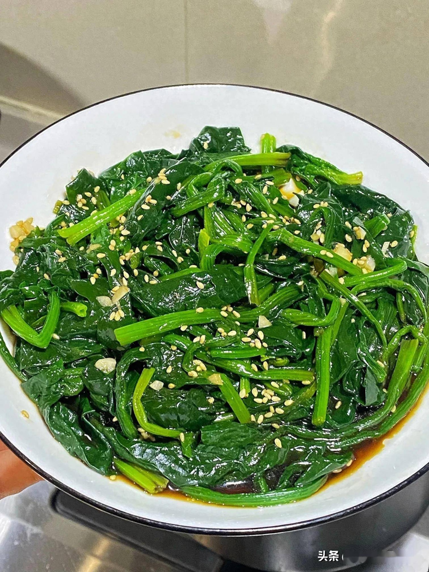 家常菜成品图：浅陶碗中盛放金橙色红薯泥基底，铺满翠绿菠菜段，表面撒蒜末与黑芝麻，淋浅金色亚麻籽油光泽，背景为原木餐桌与竹制餐具