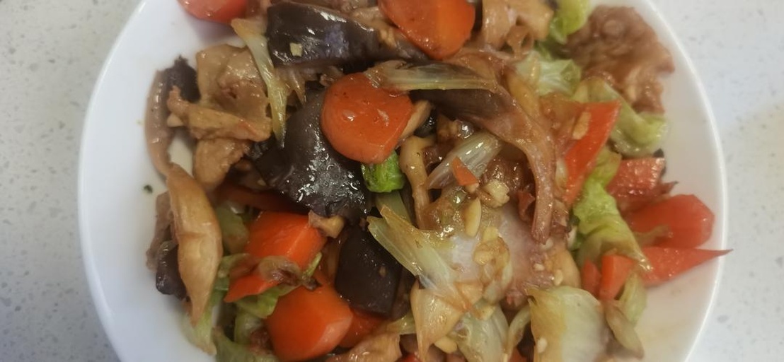 成品菜肴特写：深紫色茄子条与浅绿包菜丝交织，表面泛着油亮光泽，点缀红色辣椒片，盛放在浅色圆盘中，背景虚化突出食物主体