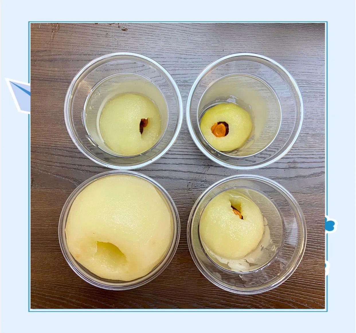 一碗透明陶瓷盅中盛放着一只完整的炖煮雪梨,梨皮呈淡黄色,内部凹陷处填充着浅褐色川贝粉末与融化的冰糖晶粒,汤汁清澈微黄,旁边放置一把小勺,背景为木质餐桌与中式厨房布景 川贝炖雪梨成品展示