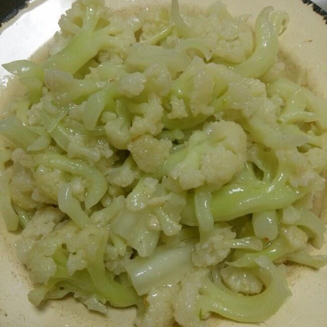 白花椰菜清炒(左)与黄心花椰菜橄榄油快炒(右)烹饪方式对比图:强调不同营养素所需的最优热处理与油脂搭配,体现科学烹饪指导价值 家庭厨房烹饪对比:左半图展示白花椰菜切块后用少量水清炒,锅中蒸汽升腾;右半图展示黄心花椰菜块与橄榄油、蒜末同炒,油面泛起金黄色光泽;两道菜均盛于浅灰釉瓷盘,突出食材本色
