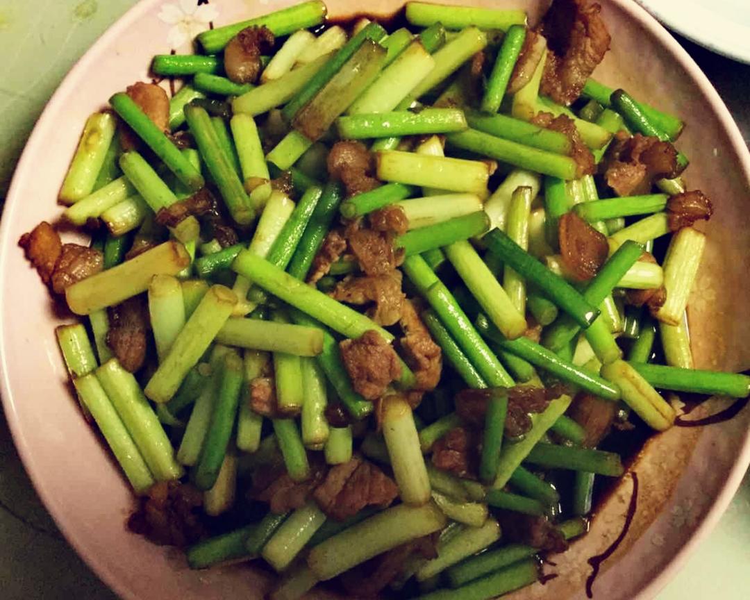 蒜薹家常养生烹饪实景:铁锅明火快炒,蒜薹段(长约3 cm)与里脊肉片(厚度0.2 cm)比例2:1,出锅前撒入鲜百合瓣6片、宁夏枸杞8粒,展现微温食材的体质适配性加工方法 家庭厨房场景:不锈钢锅中蒜薹与瘦肉片同炒,色泽翠绿油亮,锅边配放切好的百合片与枸杞,体现‘温凉制衡’烹饪智慧