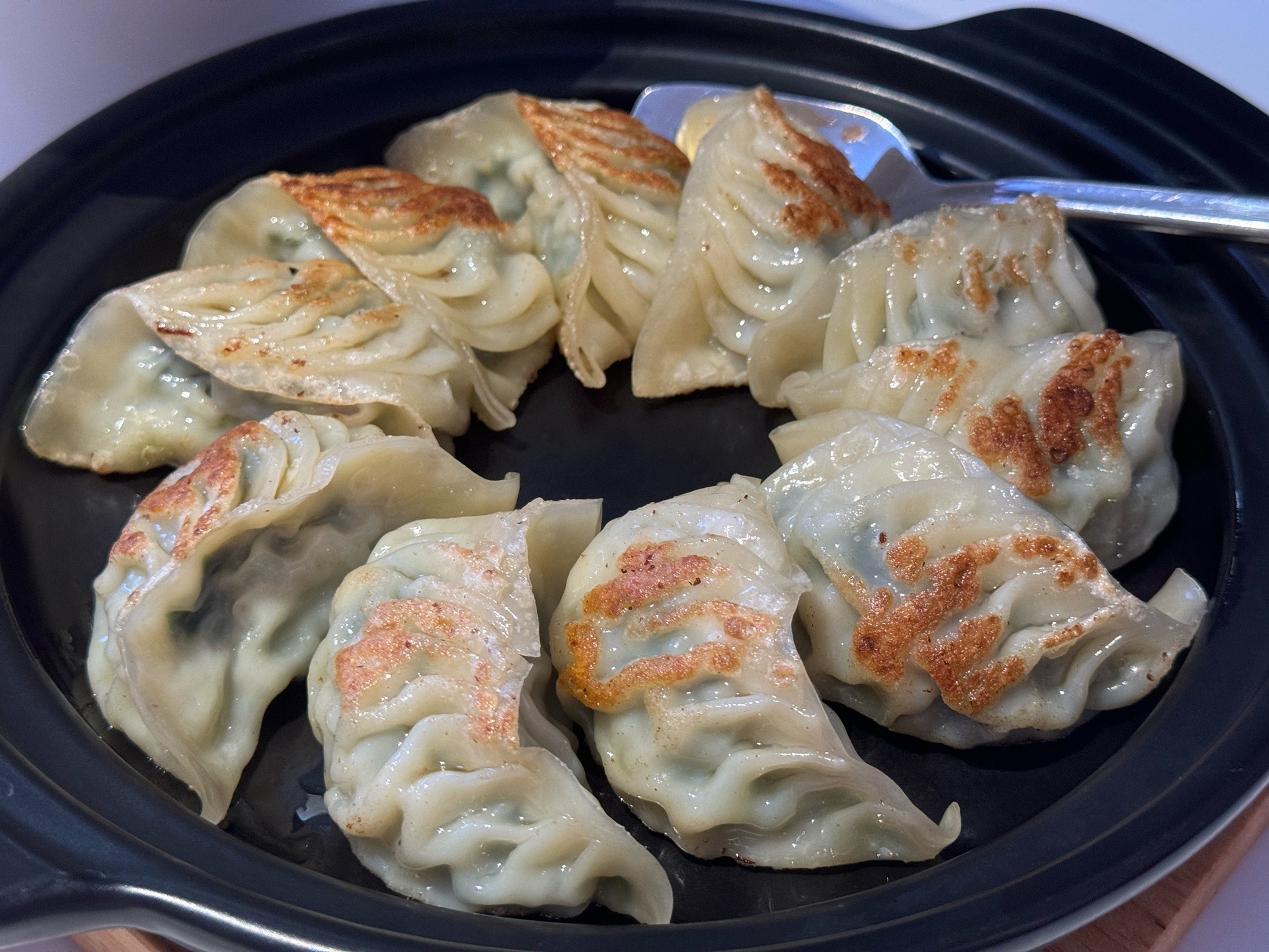 白萝卜猪肉煎饺成品图:突出‘底脆、边韧、顶软、馅亮’四重质感,展现诱人食欲与专业出品标准 成品白萝卜煎饺俯拍图:6只金黄微焦饺子呈扇形排列,底部酥脆泛琥珀光泽,顶部褶皱清晰,隐约透出浅米白色馅心,周边点缀几粒黑芝麻与香菜叶