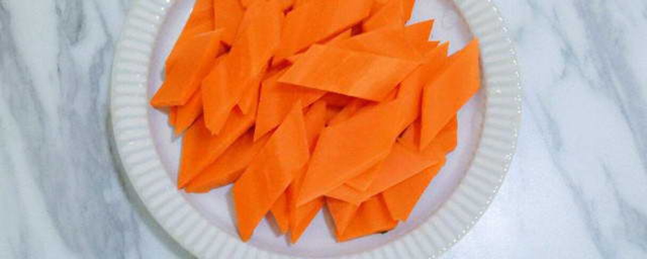 一颗被横向切开的三红胡萝卜放置在白色瓷盘中,切面完整展示出由外至内一致的深红色组织结构,纹理细腻,水分充足,旁边摆放一把不锈钢小刀和一片柠檬作为点缀,背景为浅灰色大理石台面 三红胡萝卜切面细节图