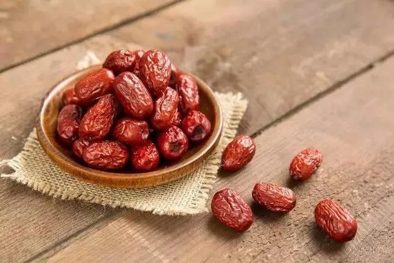 一盘铺开的琥珀色干红枣片,表面光滑有光泽,背景为木质托盘和麻布材质,展示自然健康的食品氛围 干红枣片特写