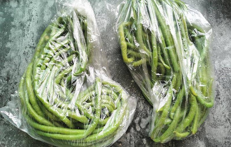 多个透明密封袋中装有焯水后冷冻的长豆角段,袋子上贴有标签注明‘长豆角-20250405’,整齐排列在冷冻抽屉中 冰箱冷冻室内分装好的豆角冷冻包