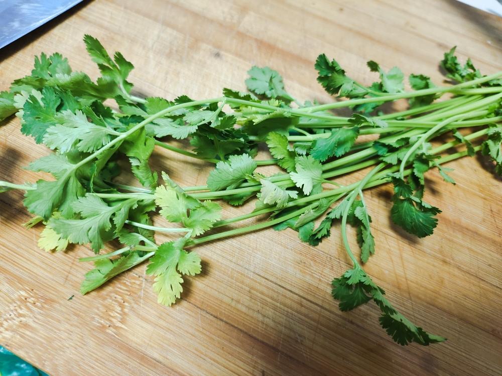 一位厨师正在将新鲜香菜切碎,准备加入汤碗中,案板上有完整的香菜束,背景为明亮整洁的现代厨房,体现香菜作为食材的日常应用 香菜在厨房中的使用场景