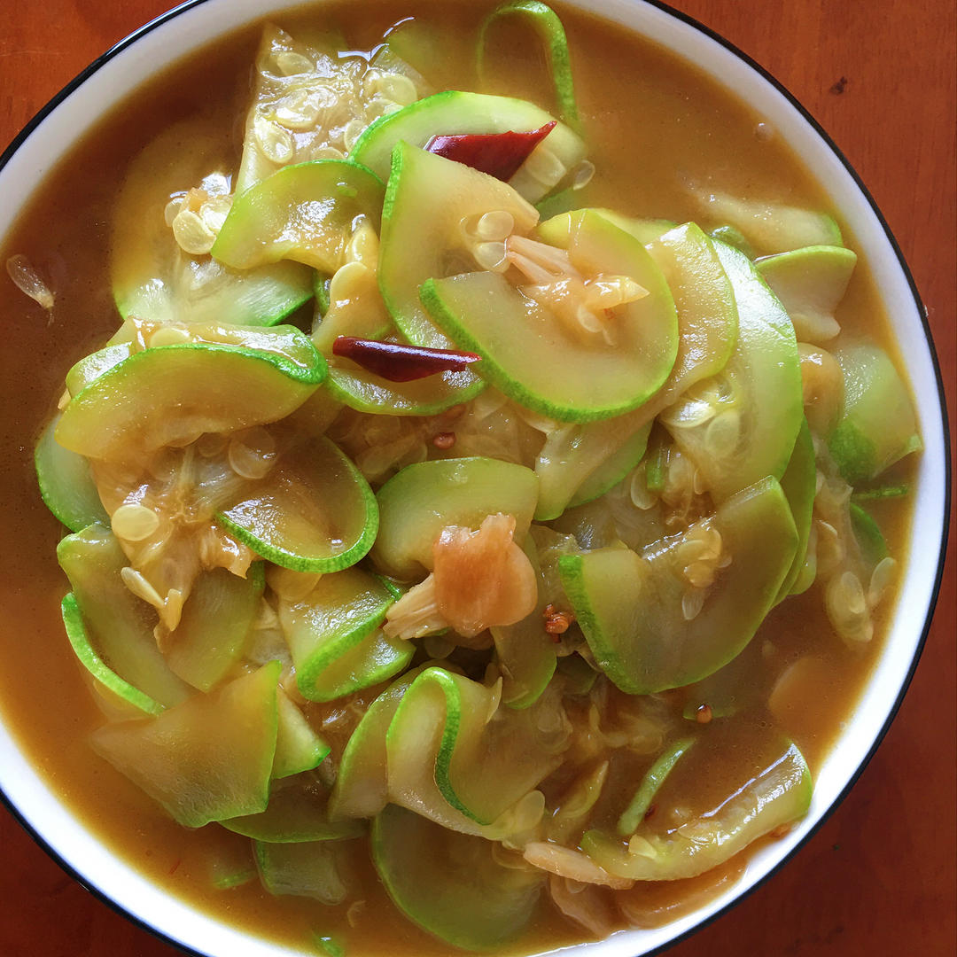 中式家常菜特写:清炒西葫芦片装于青釉瓷盘中,食材呈现半透明翠绿色,片形均匀厚薄适中,表面泛轻油光,点缀几粒红椒丁与蒜末;旁配一小碟蒸南瓜泥(橙黄色、细腻顺滑),形成色彩与质地的对比;背景虚化为木质餐桌与竹筷,强调其作为独立蔬菜的日常烹饪地位,而非南瓜替代品 西葫芦家常菜肴摆盘图