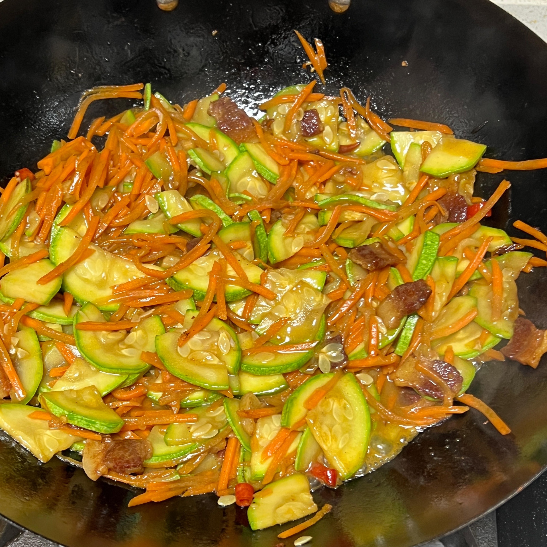 一位家庭主妇正在厨房中翻炒锅中的西葫芦块,锅具为不粘平底锅,旁边放有切好的蒜末和青葱,灶台整洁,体现健康家常烹饪氛围 家庭烹饪西葫芦菜肴场景