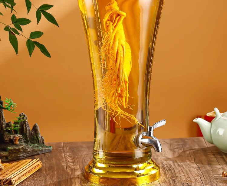 一个透明玻璃泡酒瓶内装有金黄色酒液,瓶底可见浅褐色西洋参片,旁边放置一小碗过滤用的咖啡滤纸和漏斗,背景为厨房木质台面,光线温暖 西洋参泡酒过程图