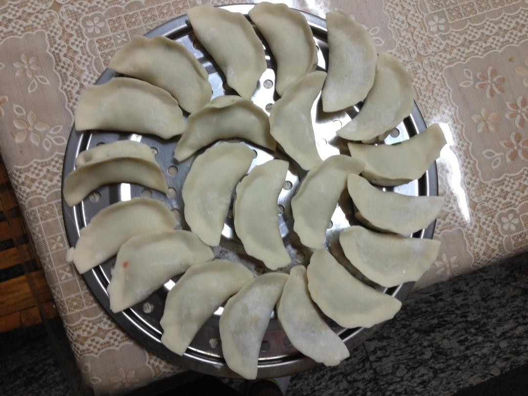 一组刚出锅的白色饺子整齐排列在竹制蒸笼上,热气腾腾,其中一个被夹起露出绿色带肉粒的馅心,旁边配有酱油碟和辣椒油,背景为厨房环境 刚出锅的蒸莴苣饺子特写