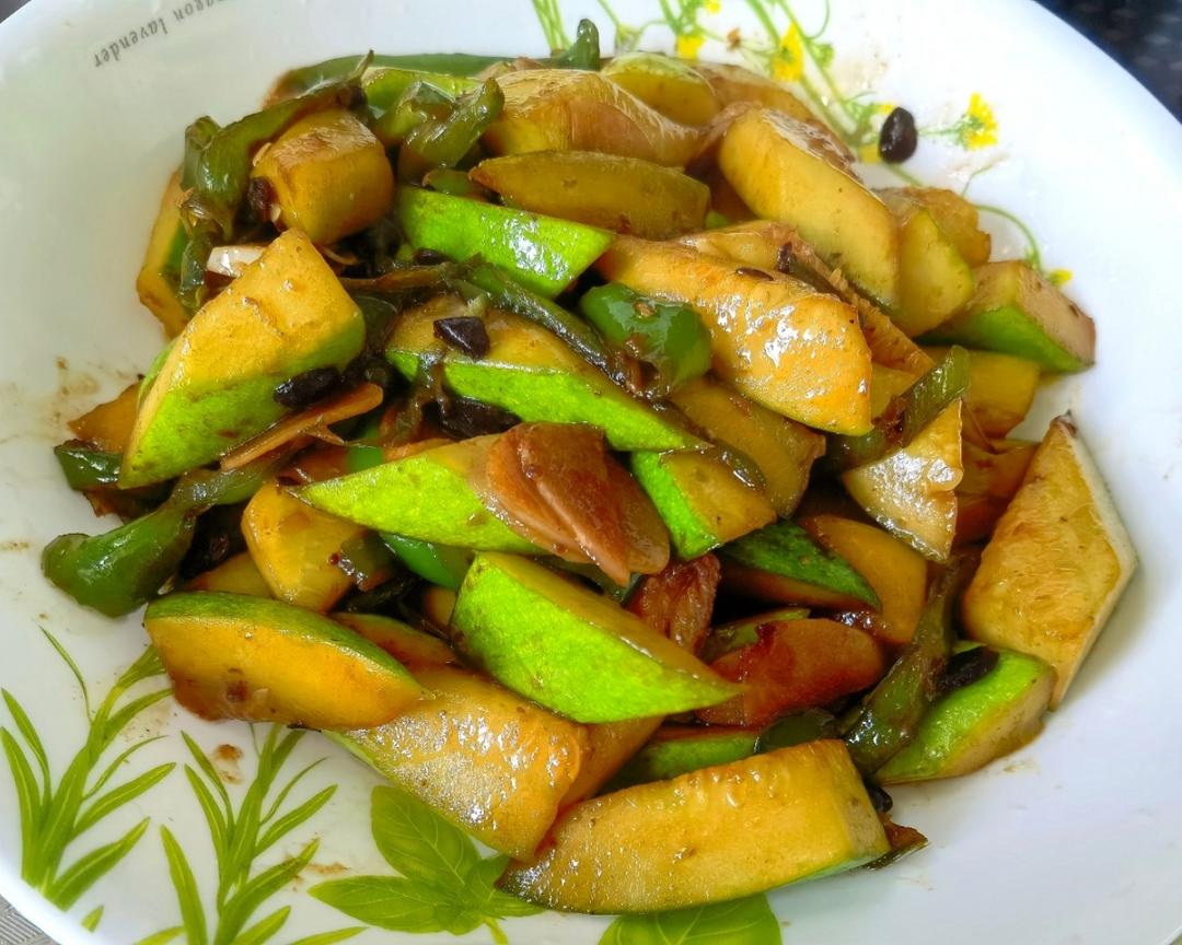 一张木制餐桌上的瓷盘里盛着一盘清炒地瓜叶,颜色碧绿油亮,点缀几瓣蒜片,旁边放着粗陶碗和竹筷,背景为传统农舍厨房,体现乡土风味 农家餐桌上的一盘清炒地瓜叶