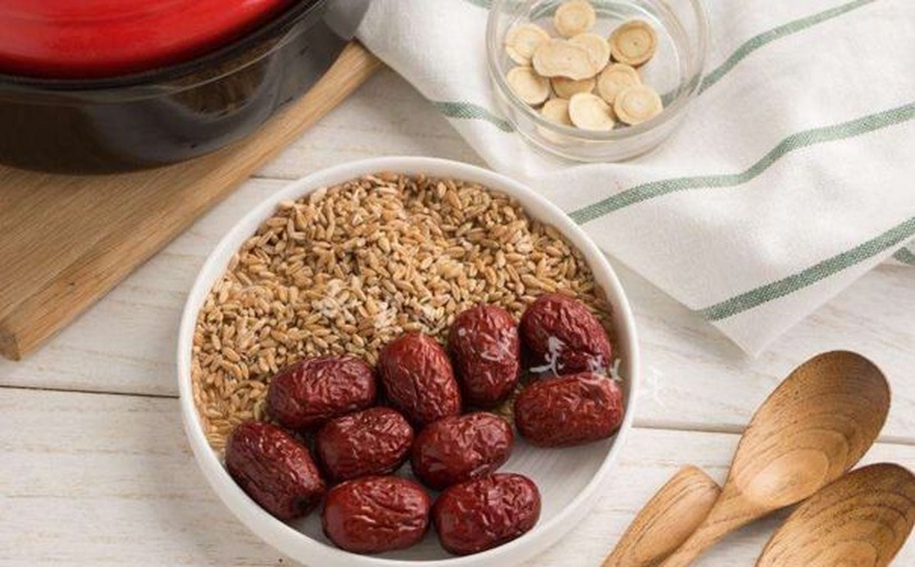 生活化场景图:一位亚洲女性坐在阳光充足的厨房桌旁,手拿一小碟干红枣片正在食用,旁边放有一杯温水和记录本,展现健康生活方式,背景模糊显示绿植和窗景 女性食用干红枣片场景