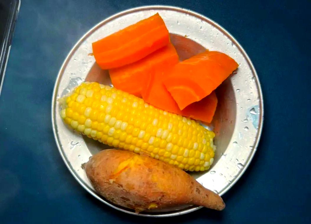 高压锅蒸屉上同时摆放蒸熟的土豆、红薯、玉米和南瓜块,色彩丰富,蒸汽缭绕,体现多样化的健康主食组合 多种根茎类蔬菜共蒸图