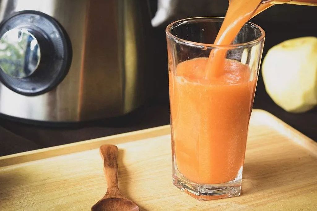 厨房台面上摆放着切开的甜橙、玻璃杯、量杯、搅拌棒和一瓶冷藏牛奶;一只手正在将橙汁倒入装有牛奶的透明玻璃杯中,液体呈现柔和的乳白色与淡黄色交融状态,杯壁可见细微气泡,体现新鲜调配场景 香橙牛奶饮品制作过程图