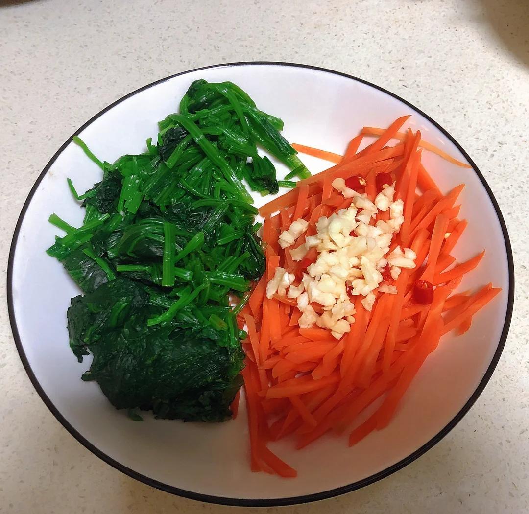 一位主妇在明亮厨房中将焯过水的大叶菠菜与红椒丝混合调味,案板上有柠檬、橄榄油瓶和蒜末,体现健康烹饪方式 家庭厨房中烹饪大叶菠菜的场景